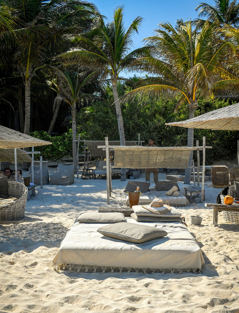 A daybed on the sand under palm trees at a Tulum beach club