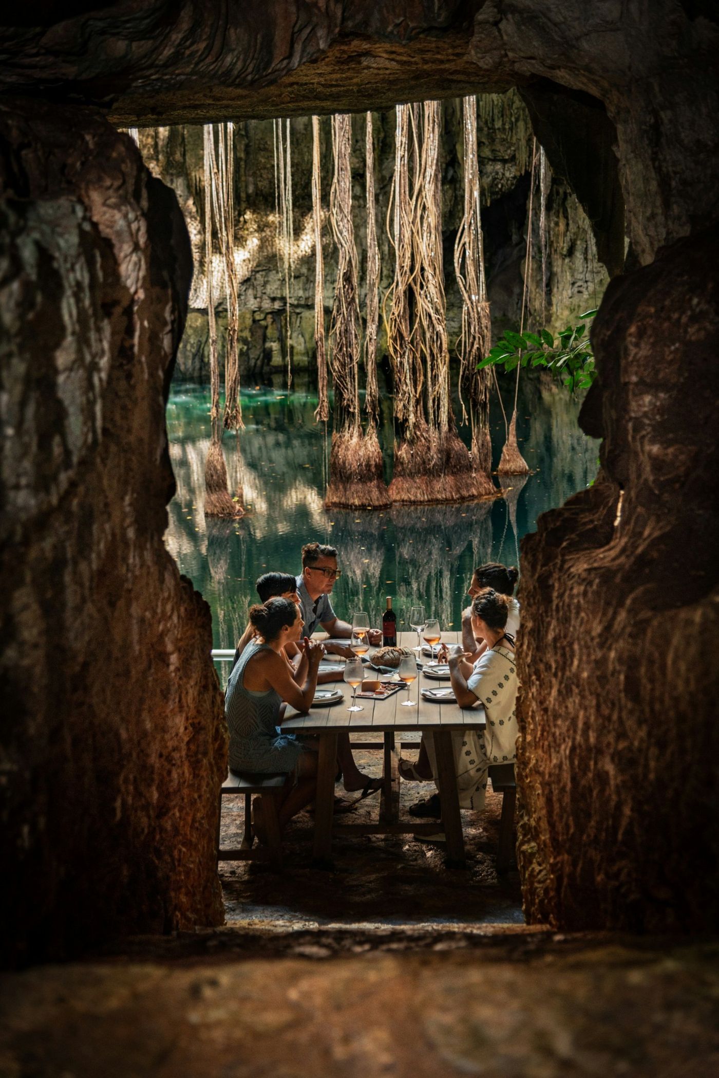 A small group at dinner beside a cenote, seen through a stone opening